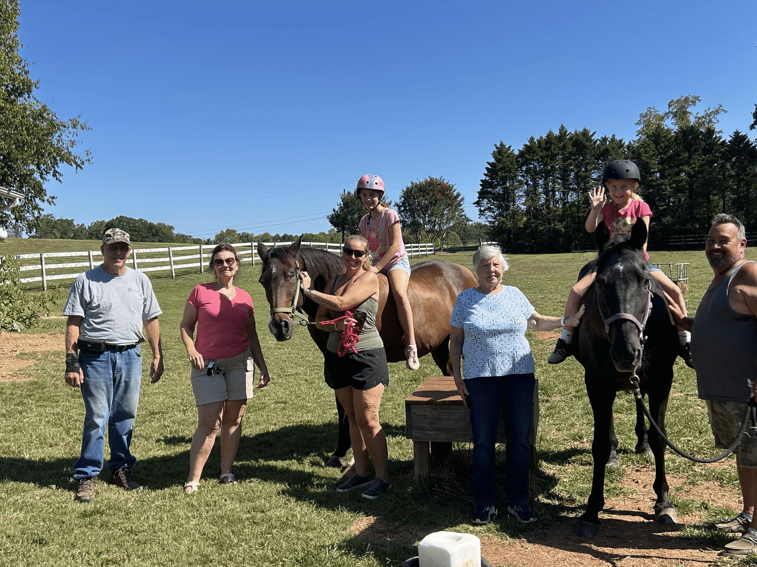 Families and caregivers with two horses at Saving Grace Healing With Horses in a fenced pasture