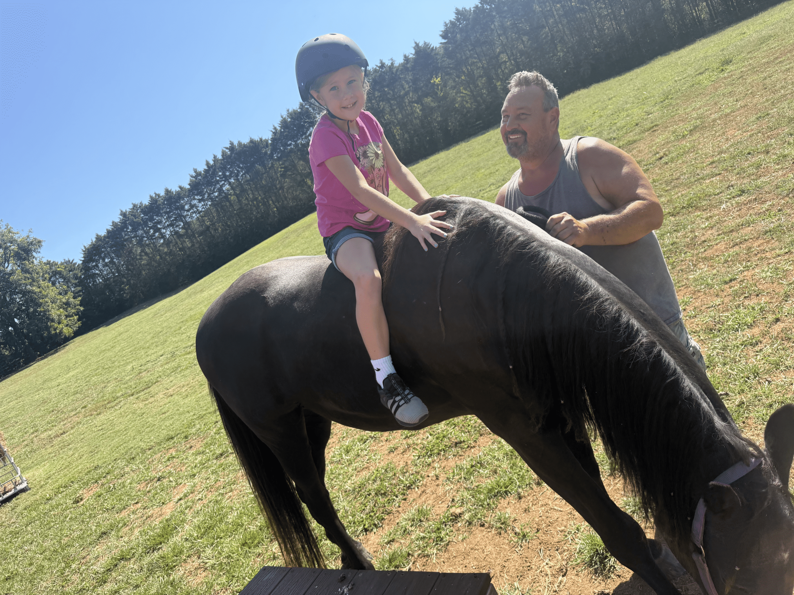 Child wearing a helmet riding a black horse with an adult supporter at Saving Grace Healing With Horses